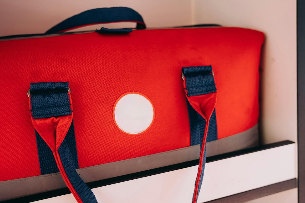 Close-up of a vibrant red duffel bag with blue straps on a shelf.